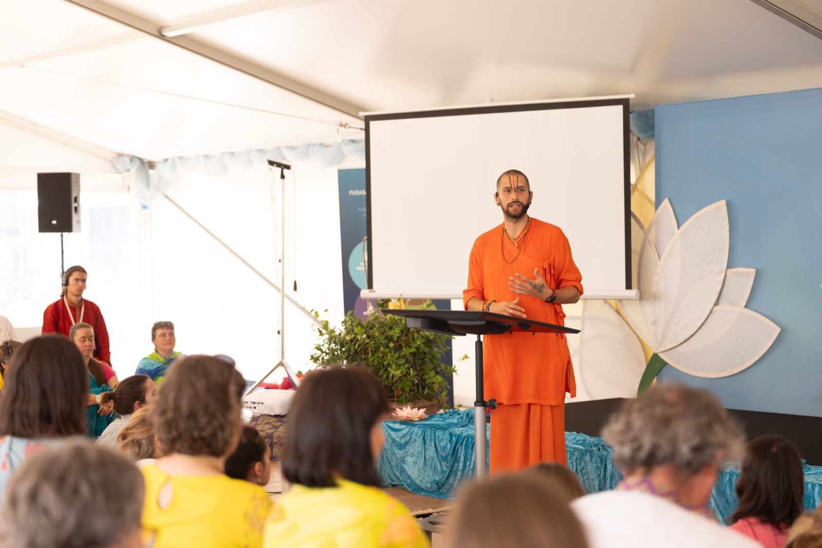 A speaker presenting to a seated audience in the event tent